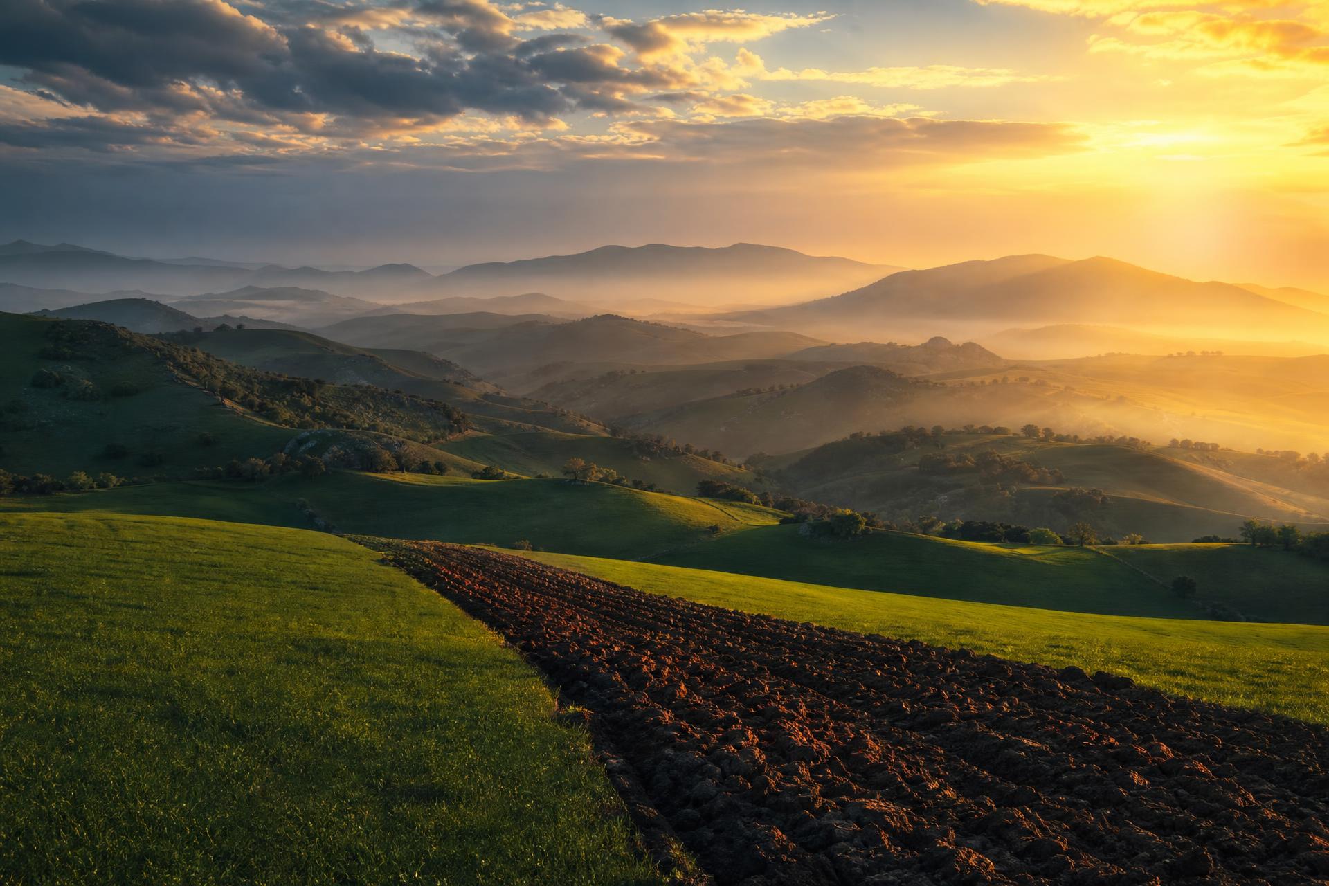 Golden hour over Northern California rolling hills with a long earthen furrow cutting toward distant blue ridges