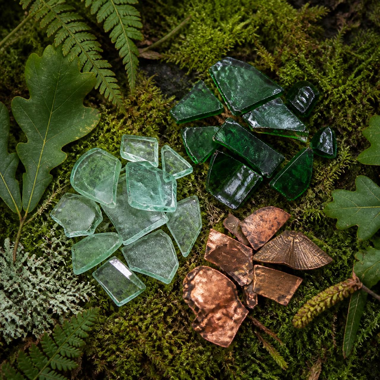 Recycled green glass and copper fragments arranged on moss and ferns